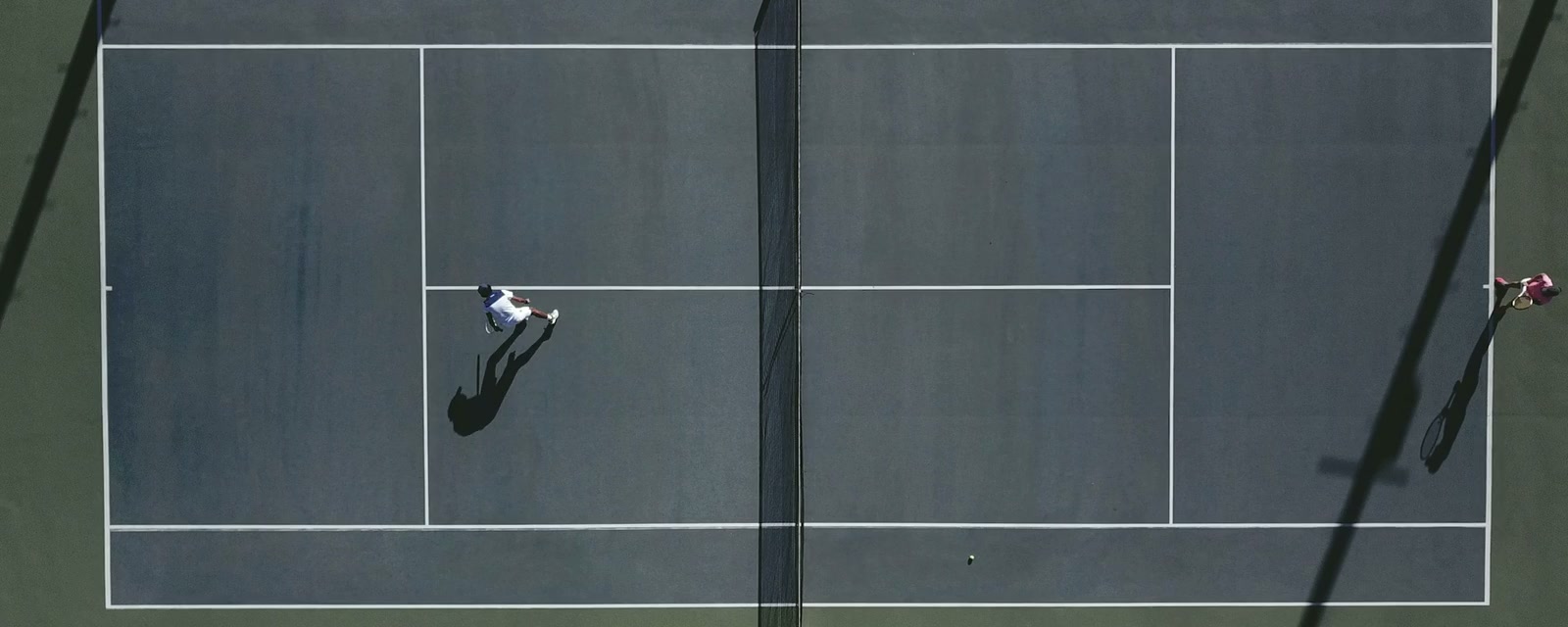 Players and long shadows seen from above a tennis court
